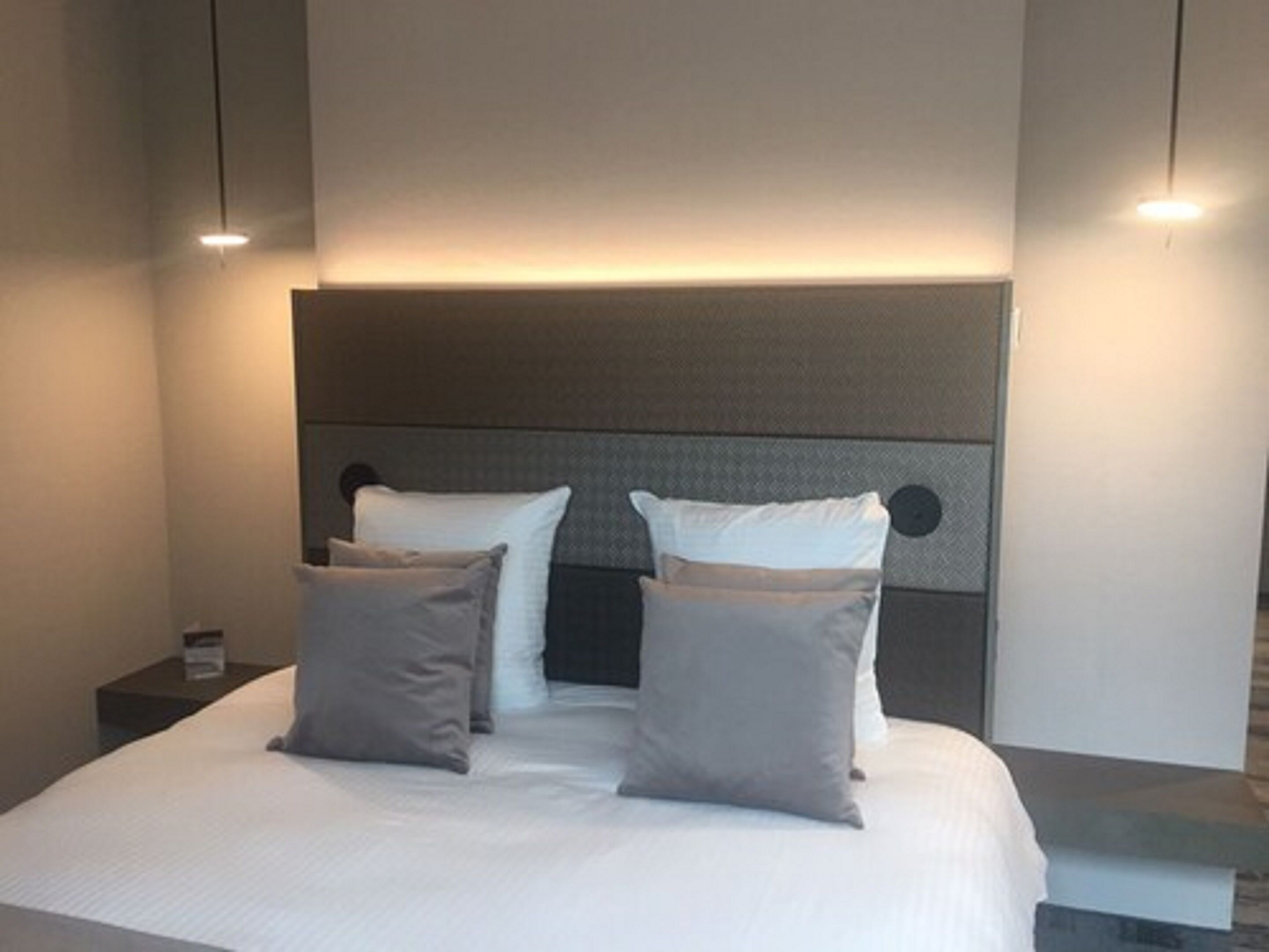 A modern bedroom with a large bed, a headboard with circular cutouts, and bedside tables with lamps.