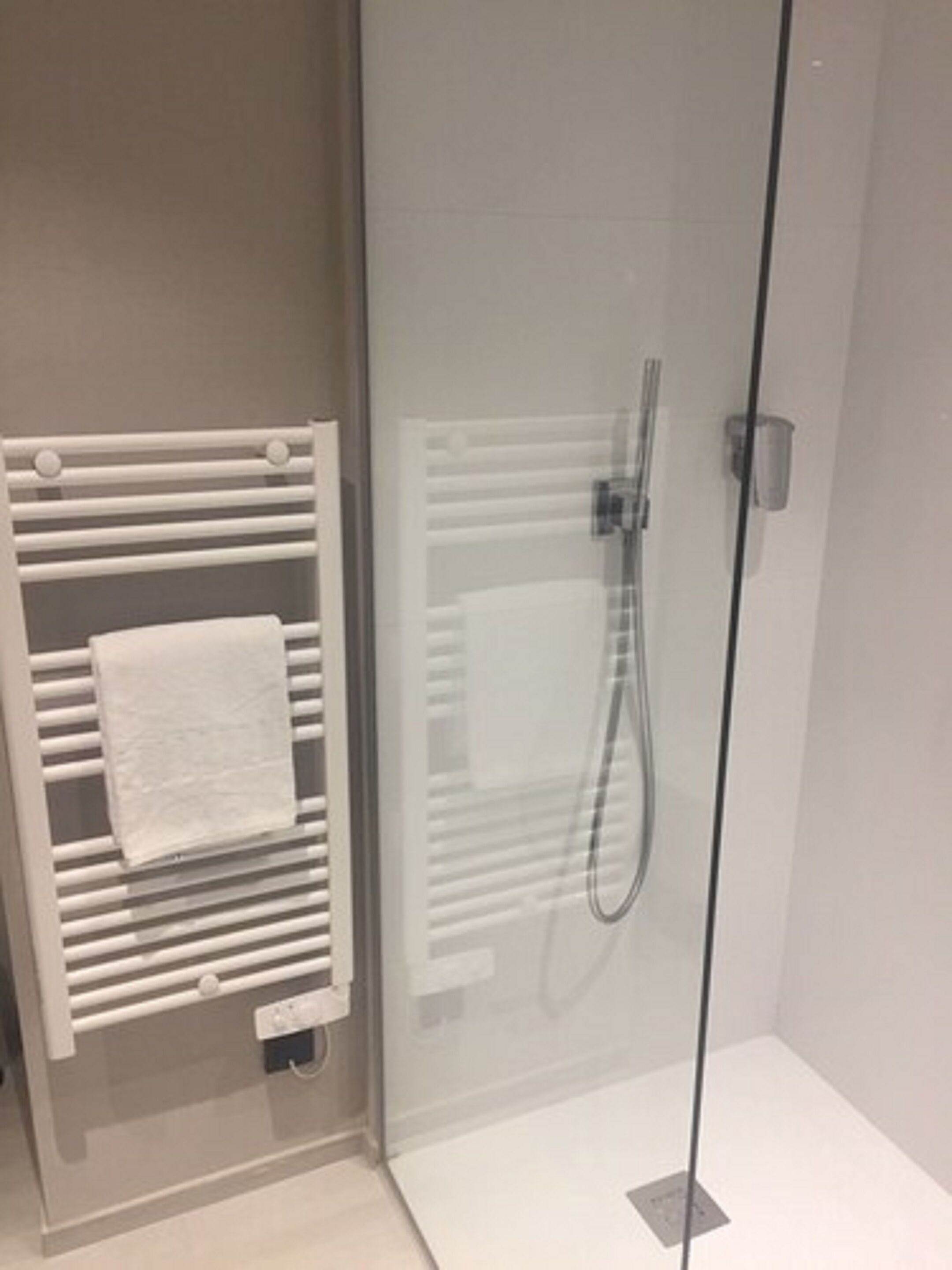 Un baño moderno con cabina de ducha de vidrio, toallero blanco y panel de control visible.