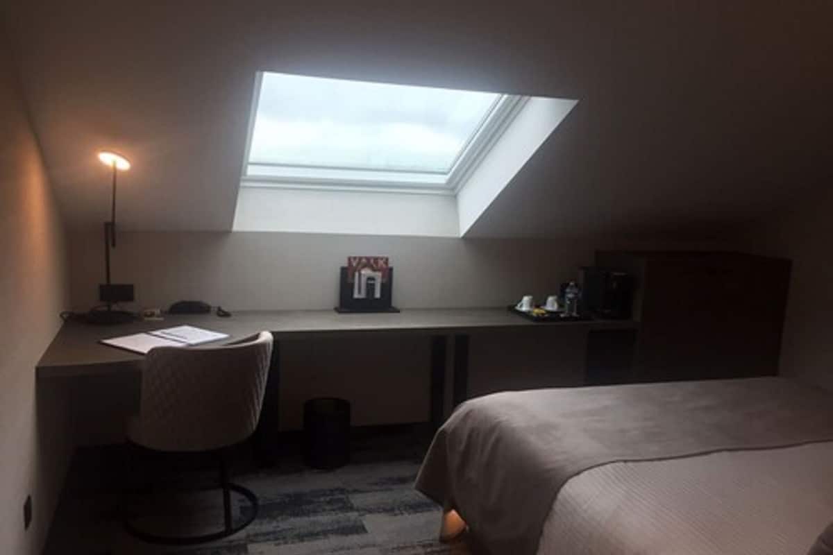 Ein kleiner Raum mit Oberlicht über einem Schreibtisch, einem Stuhl und einem Bett.