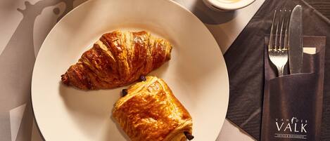 Ein Teller mit zwei Croissants und einer Tasse Kaffee auf einem Tisch, ergänzt durch eine Serviette und eine Gabel.