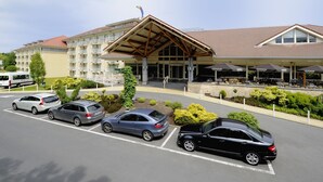 A hotel with a covered outdoor seating area, a parking lot with several cars, and a building with multiple balconies. - Van Der Valk Hotel Charleroi Airport (Charleroi)