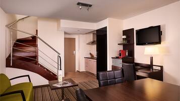 Una habitación de hotel moderna con una escalera de madera, un comedor con mesa y sillas, una cocina y un televisor de pantalla plana montado en la pared.