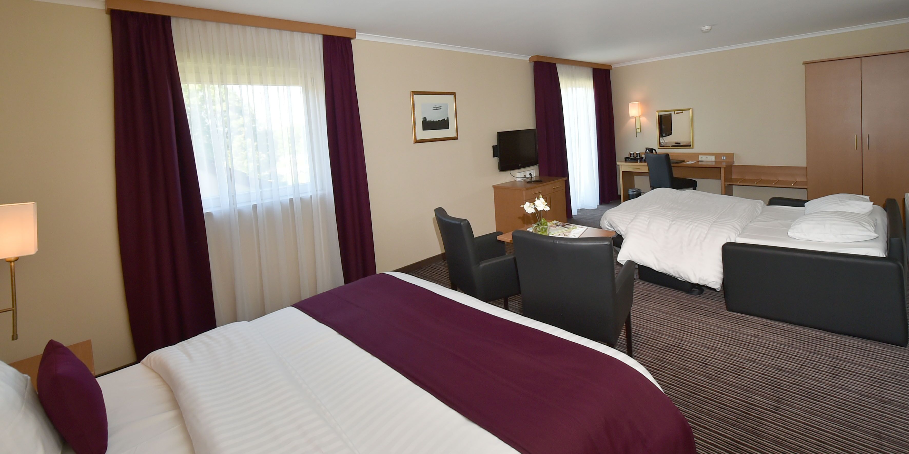 A hotel room with two beds, a desk, a chair, a television, and a wardrobe.