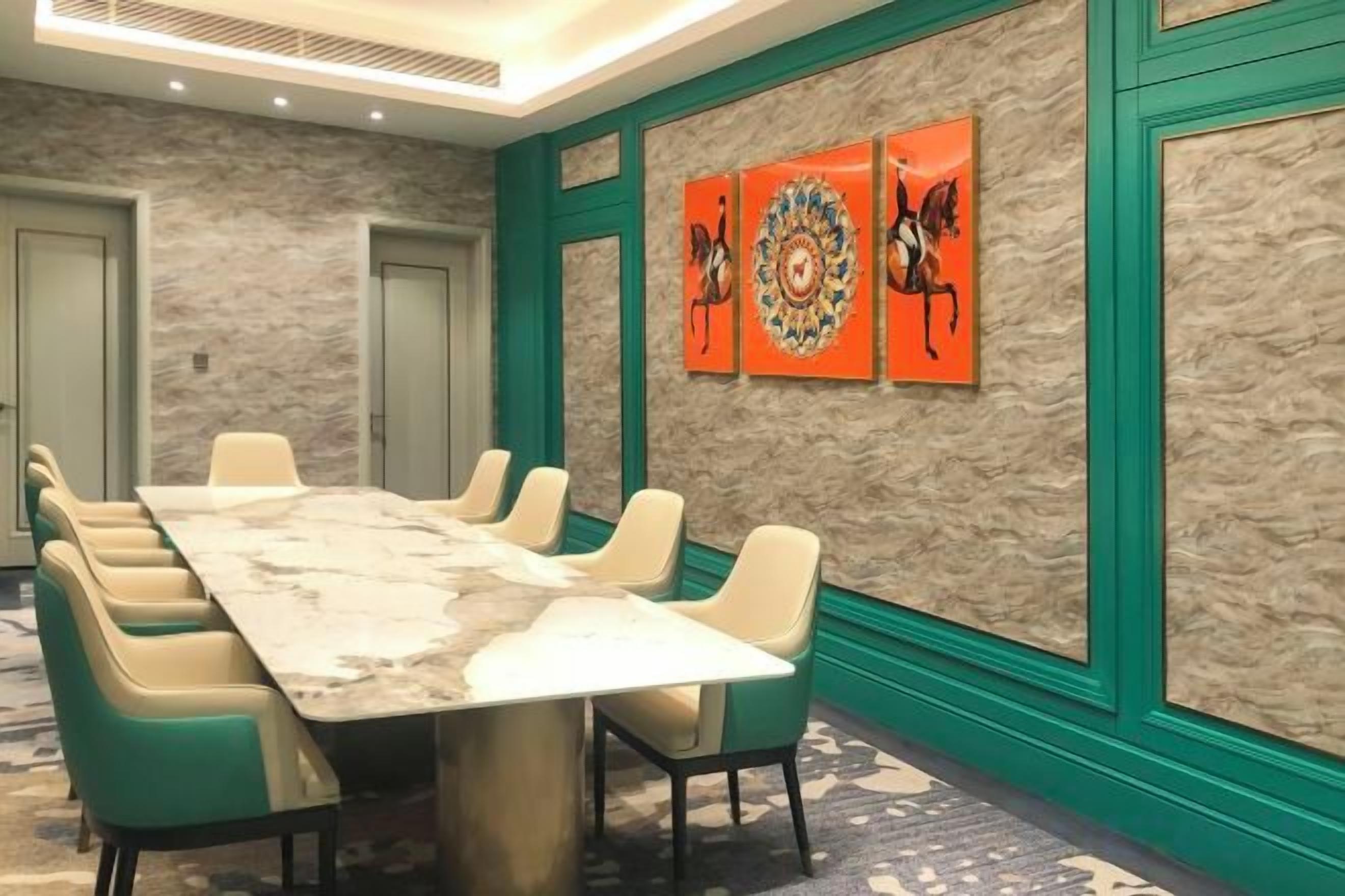 A conference room with a marble table, green chairs, and decorative wall art.