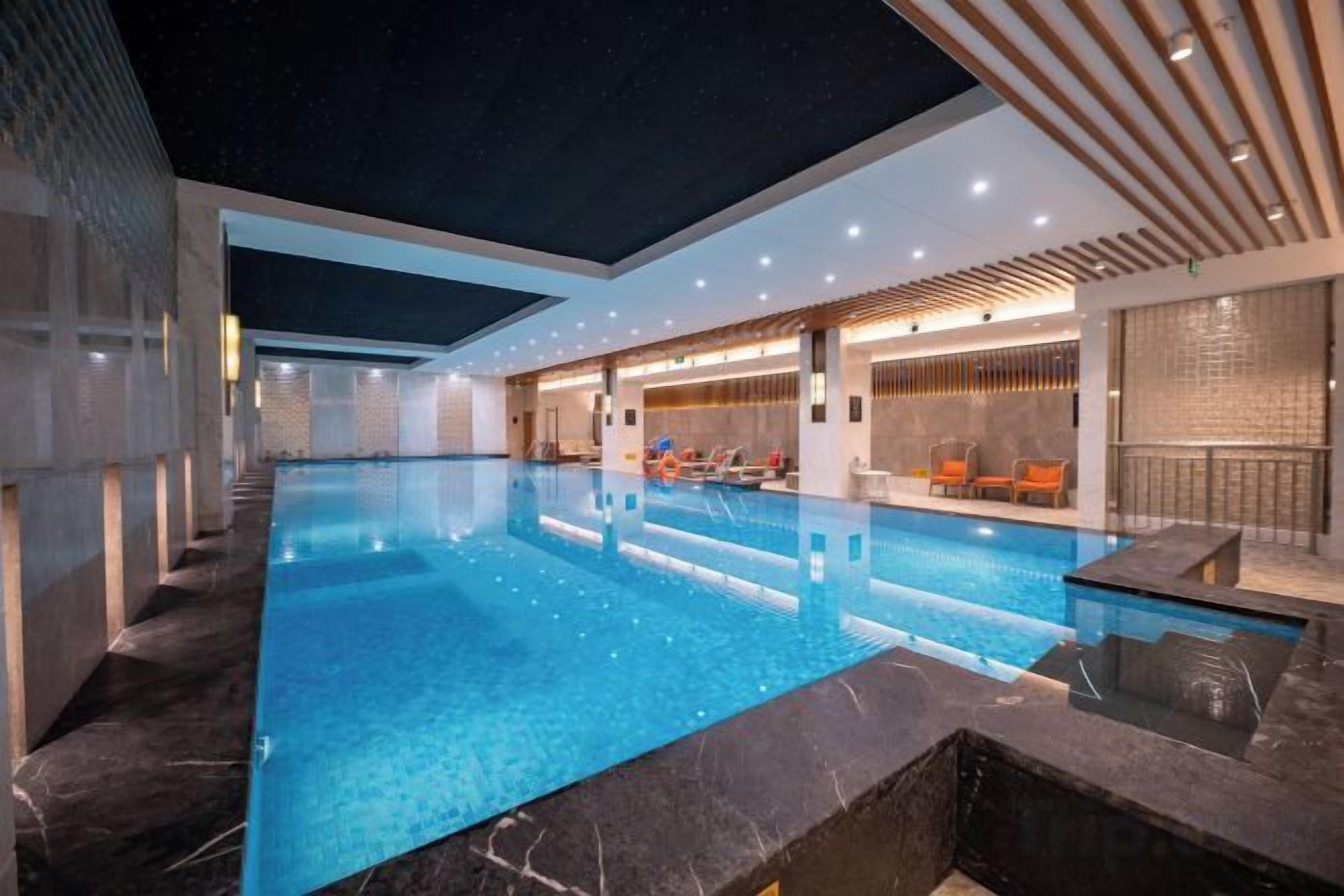 An indoor swimming pool with a clear view of the pool area, a seating area with chairs, and a modern architectural design.