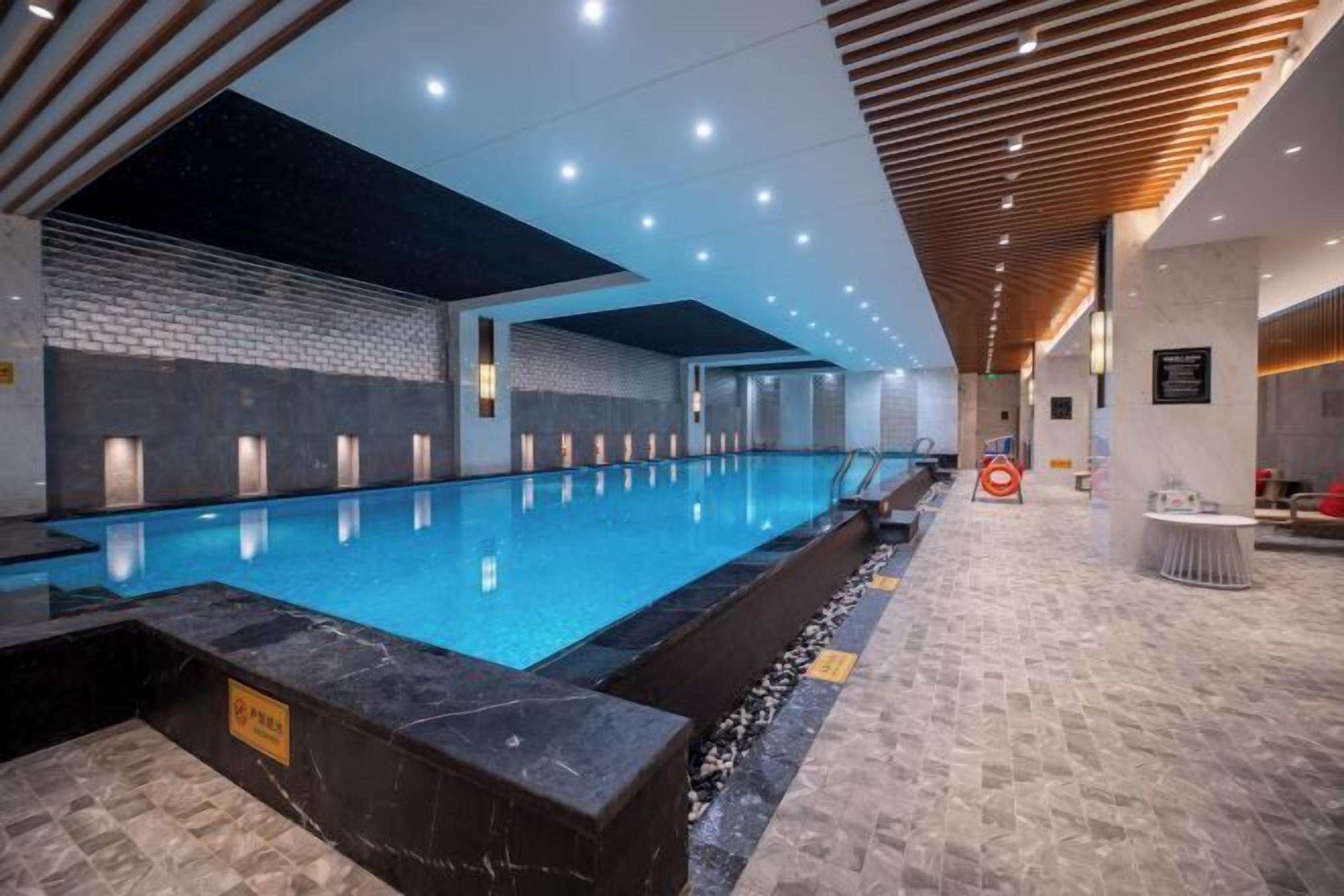 A modern indoor swimming pool with a clear water surface, surrounded by a tiled floor and a wooden ceiling.