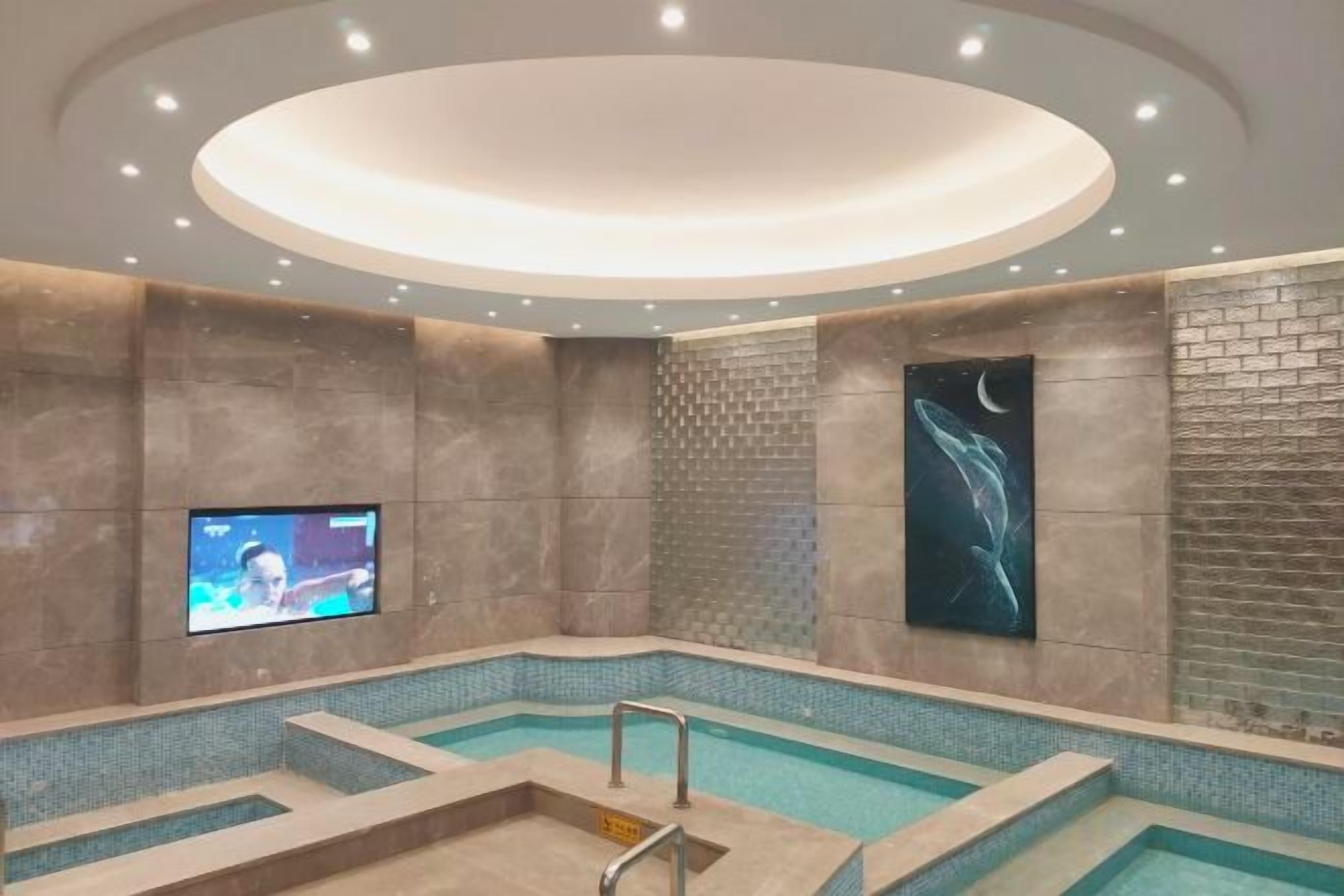A modern indoor swimming pool with a television screen, a mural, and a unique ceiling design.