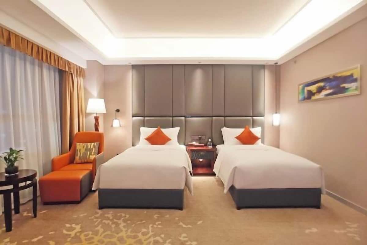A hotel room with two beds, a nightstand, a chair, a lamp, and a painting on the wall.