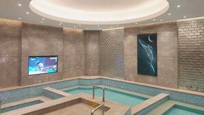 A modern indoor pool with a circular ceiling light, a television screen, and a large abstract painting on the wall. - Yinlong Hotel (Xining)