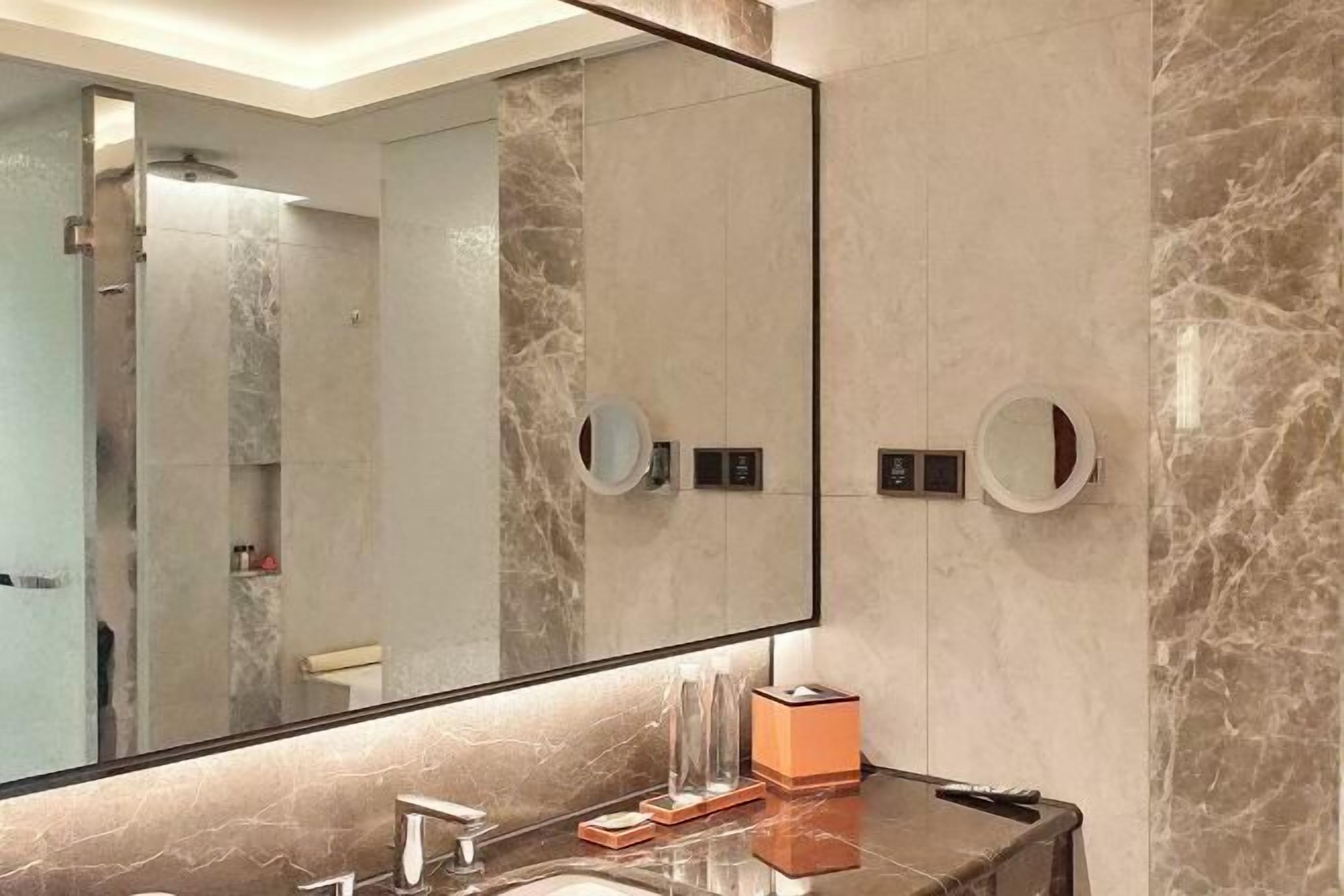 A bathroom with a large mirror, marble walls, a sink, and two round mirrors on the wall.