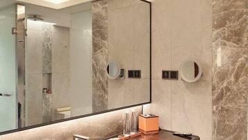 A bathroom with a large mirror, marble walls, a sink, and two round mirrors on the wall.