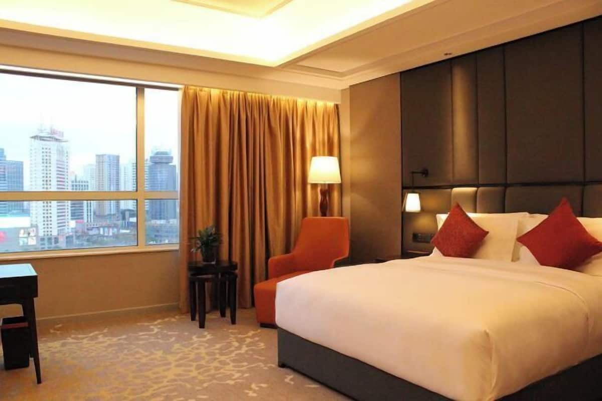 A hotel room with a large bed, a chair, a desk, and a view of the city.
