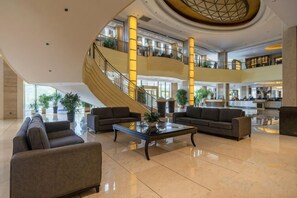 Un vestíbulo amplio con una escalera central, área de descanso y un mostrador de recepción.