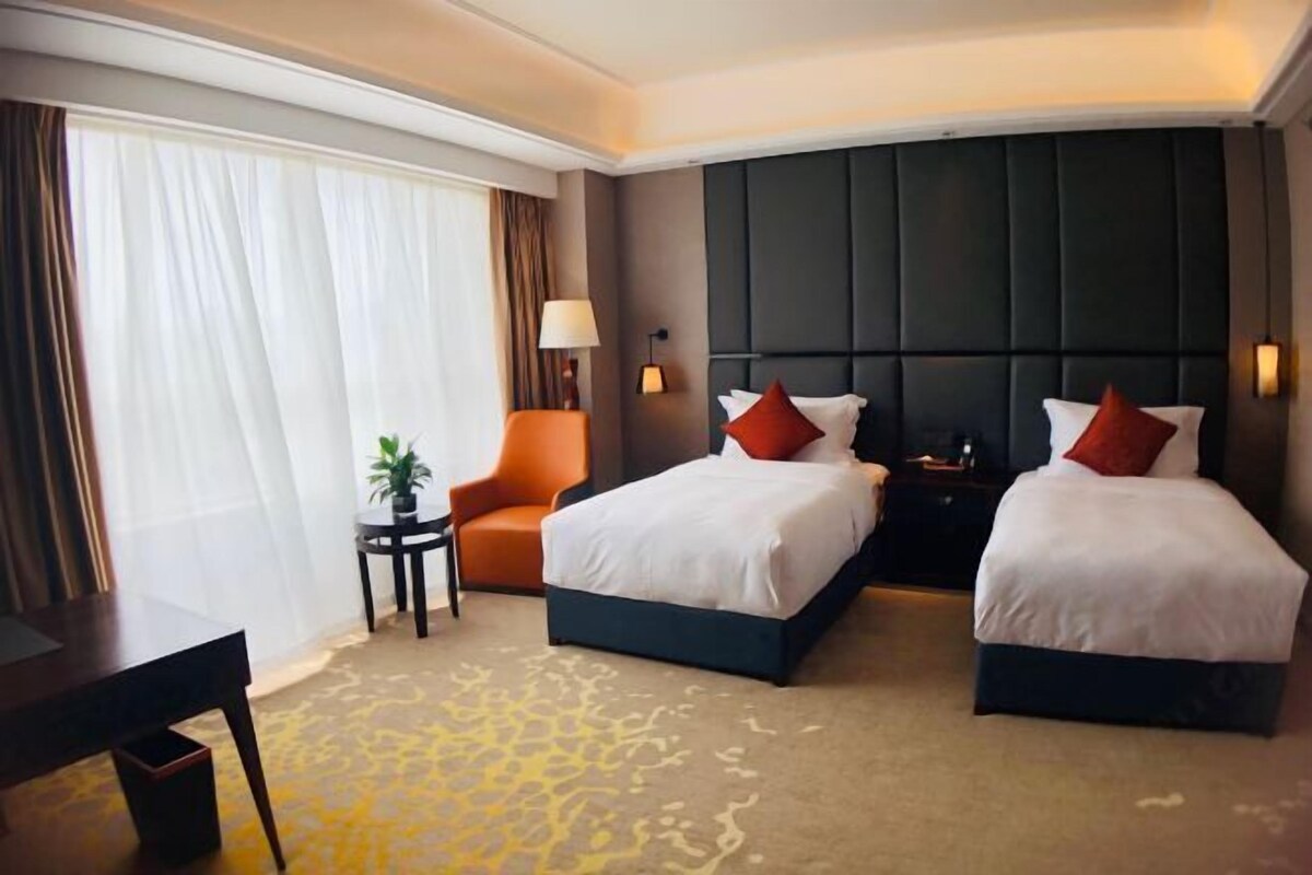 Habitación de hotel con dos camas, un escritorio, una silla, una lámpara y vistas al exterior.
