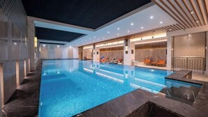 A modern indoor swimming pool with a clear blue water surface, surrounded by a lounge area with seating and a wooden ceiling design. - Yinlong Hotel (Xining)