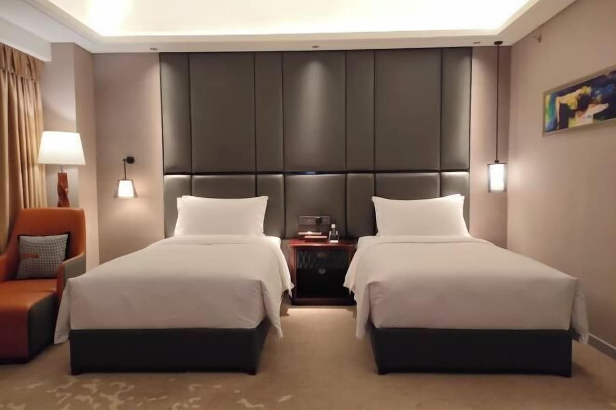 Habitación de hotel con dos camas, una mesita de noche, una lámpara y una silla.