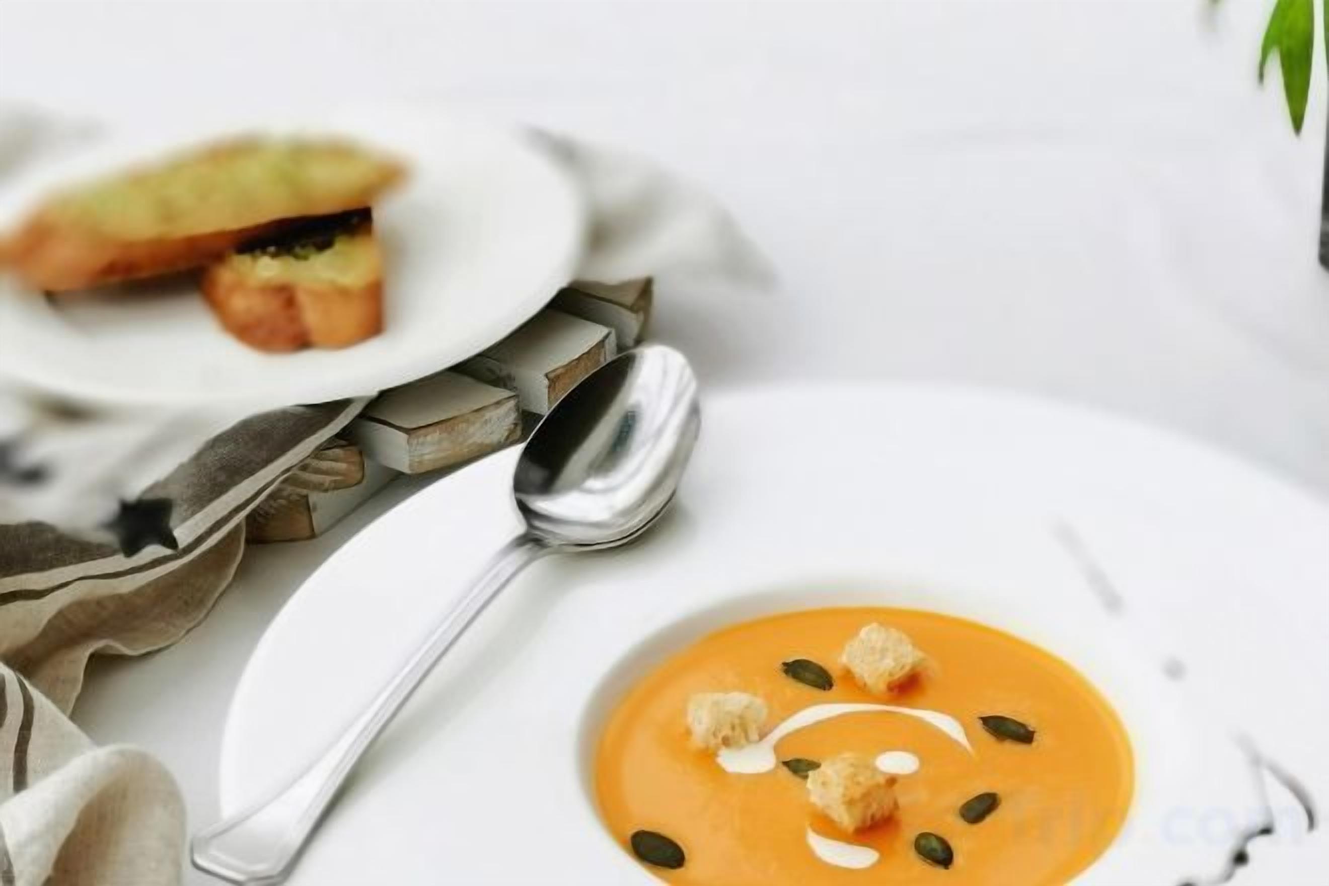 Une table à manger avec une assiette de soupe et un sandwich, accompagnés d’une cuillère et d’une serviette.
