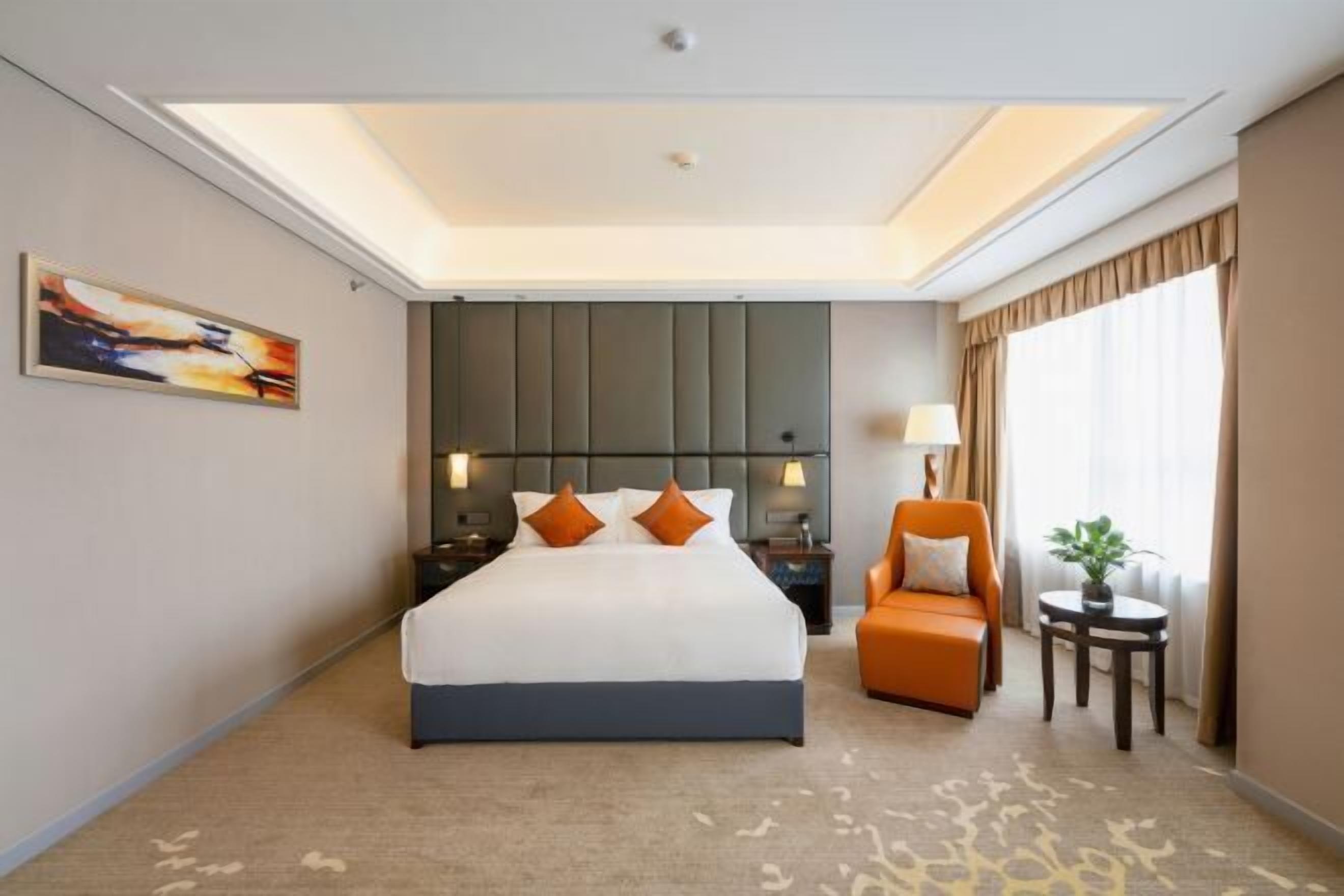 A hotel room with a large bed, a sofa, a small table, and a painting on the wall.