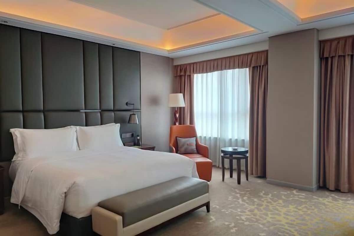 A hotel room with a large bed, a chair, a small table, and a window with curtains.