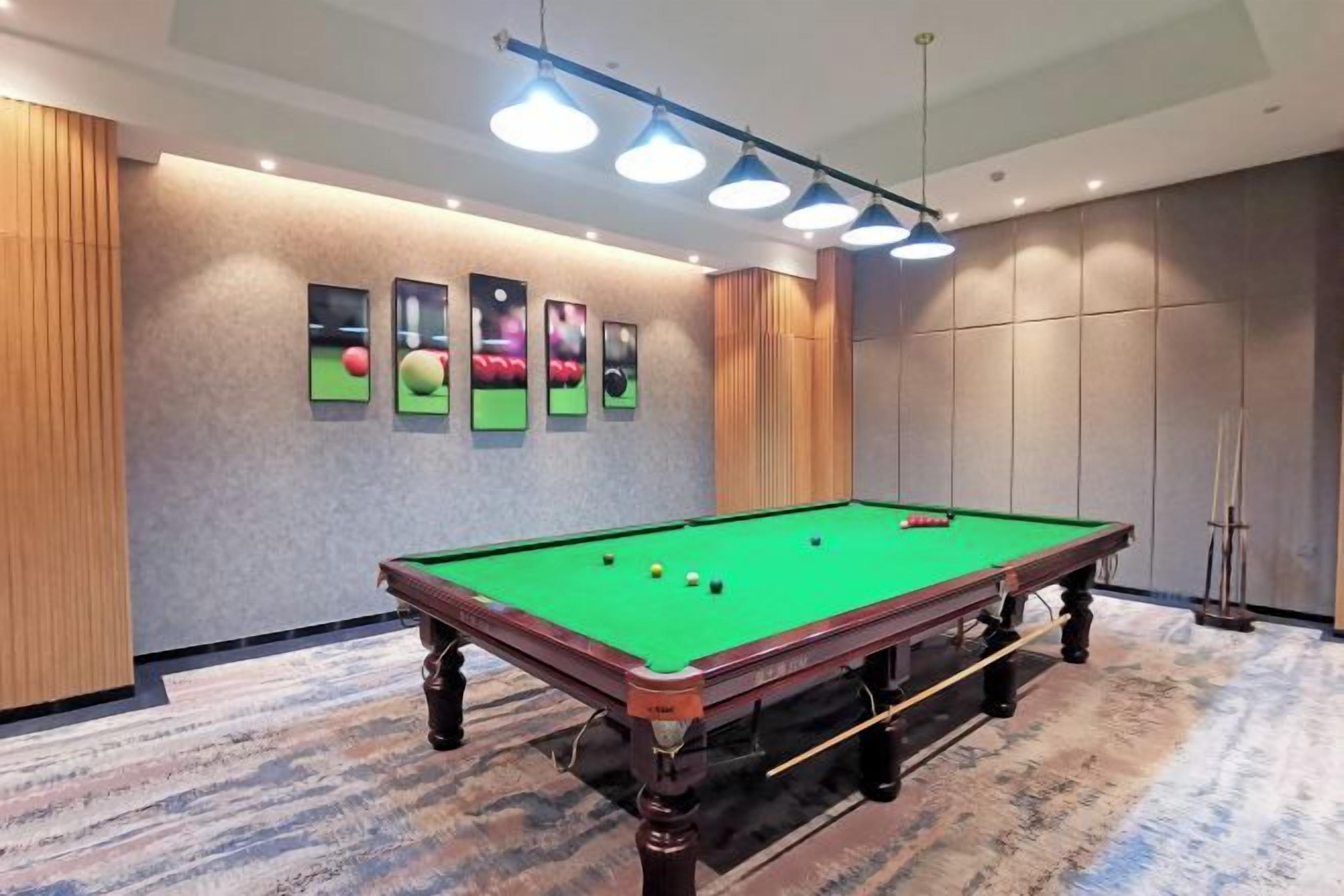 A pool table in a room with a patterned carpet, recessed lighting, and framed pictures on the wall.