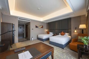 A hotel room with two beds, a desk, a chair, and a small table with a plant.
