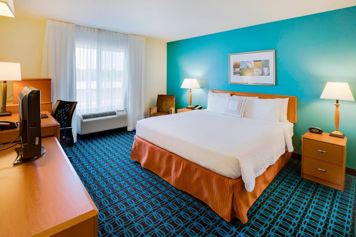Habitación de hotel con una cama grande, un escritorio con ordenador, una silla y una ventana con cortinas.