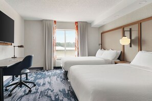 Una habitación de hotel con escritorio, dos camas, un ventanal grande con cortinas y un televisor montado.