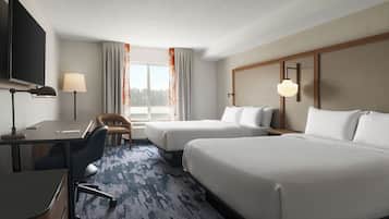 A hotel room with two beds, a desk, a chair, a TV, and a window with curtains.