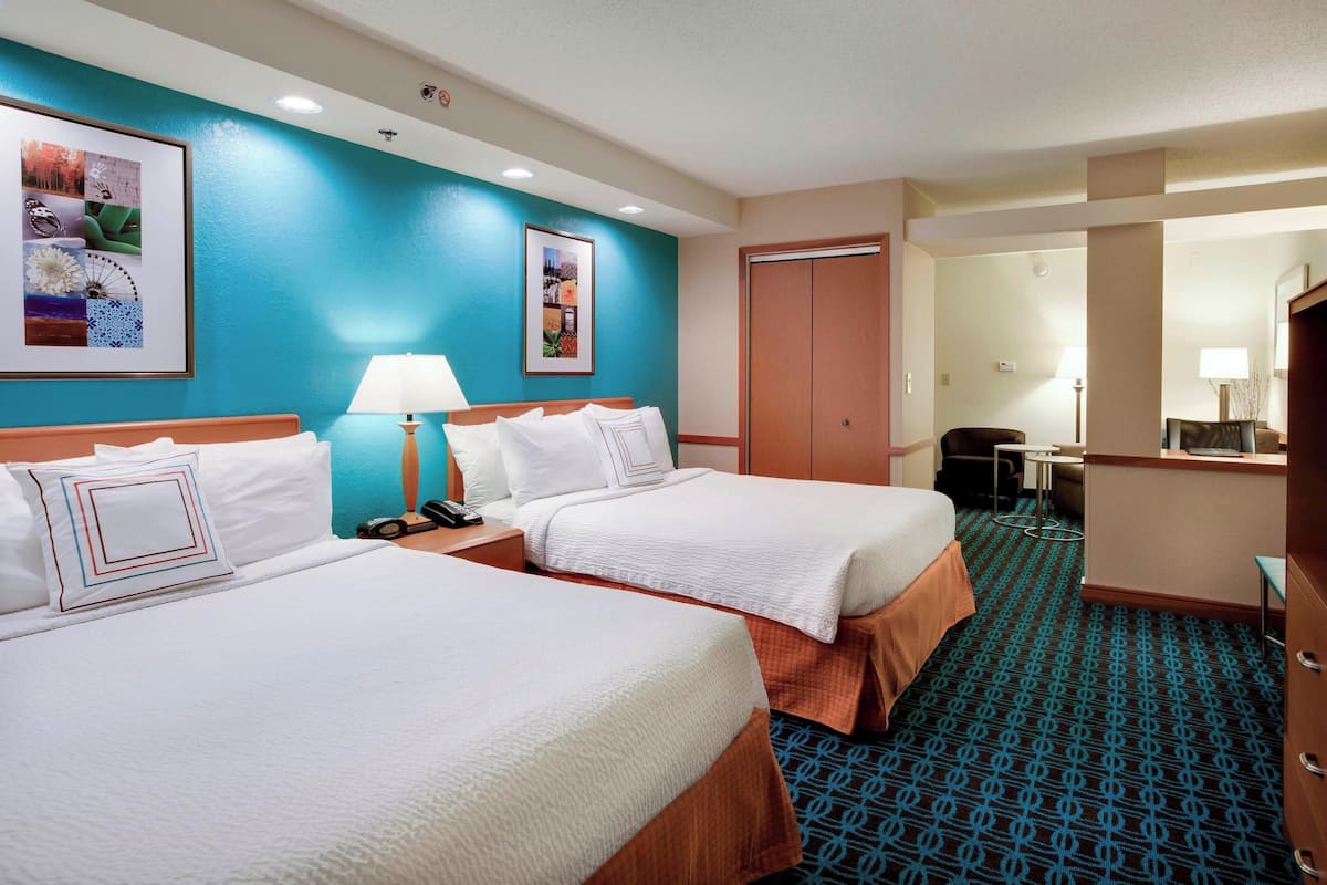 Una habitación de hotel con dos camas, un escritorio, una silla, una lámpara y un espejo.