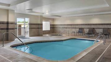 A swimming pool with a tiled deck, a hot tub, and seating area with chairs and tables.