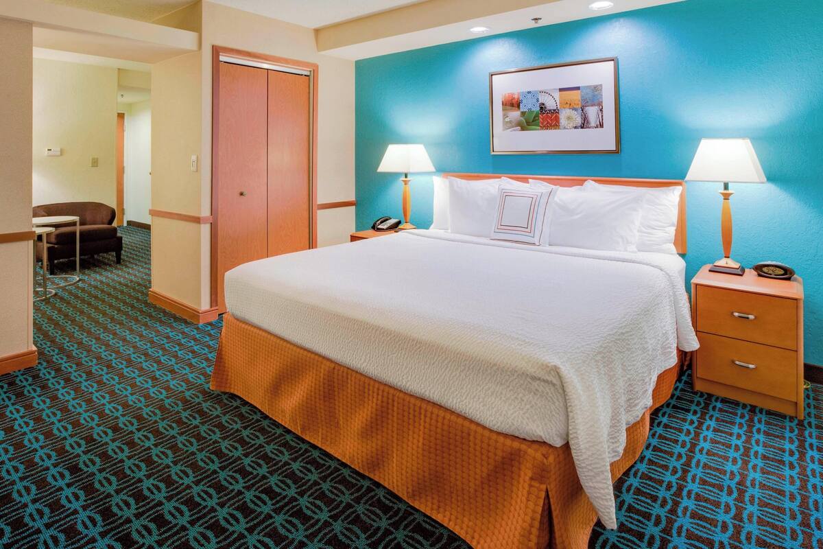 Una habitación de hotel con una cama grande, dos mesitas de noche con lámparas, una silla, un armario y una alfombra de diseño geométrico.