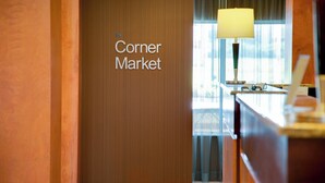 Interior de un hotel con una pared de madera que muestra el letrero de "the Corner Market", un escritorio con una lámpara y vistas al exterior a través de una ventana.