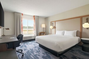 A hotel room with a bed, desk, chair, and a view of the outdoors.
