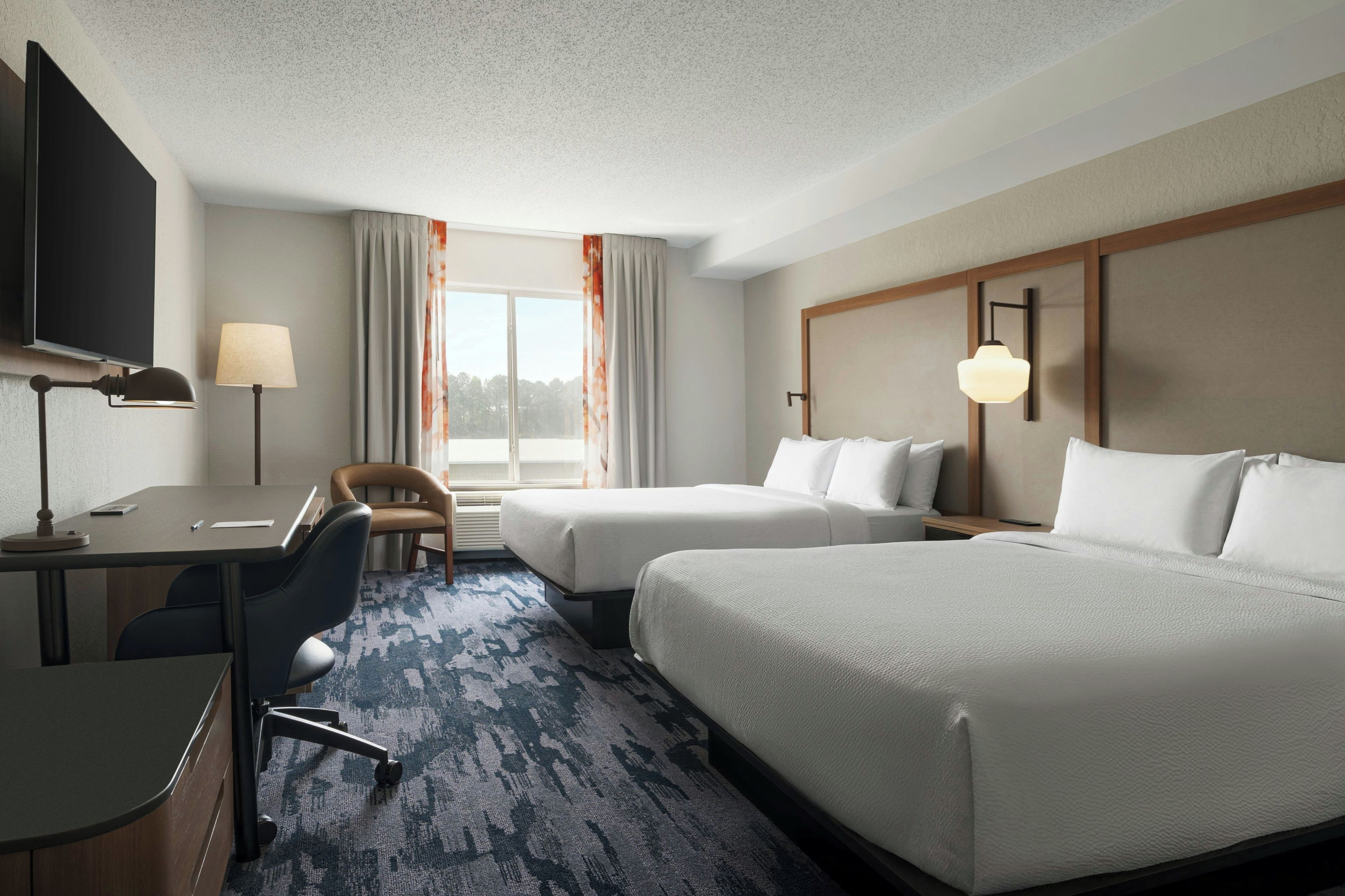 A hotel room with a desk, two beds, a chair, and a TV.