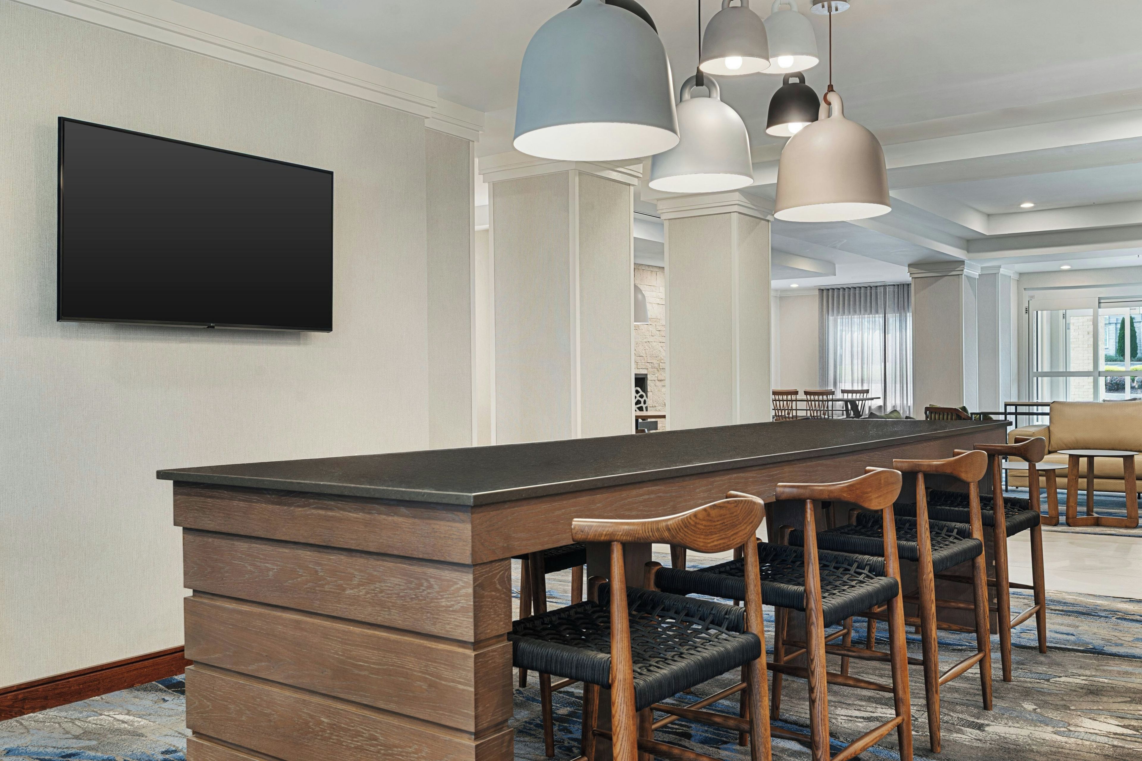 A hotel dining area with a long table, multiple chairs, and pendant lighting.