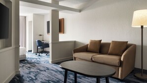 Una habitación de hotel con sofá, una mesita, lámpara, televisor y escritorio con silla.
