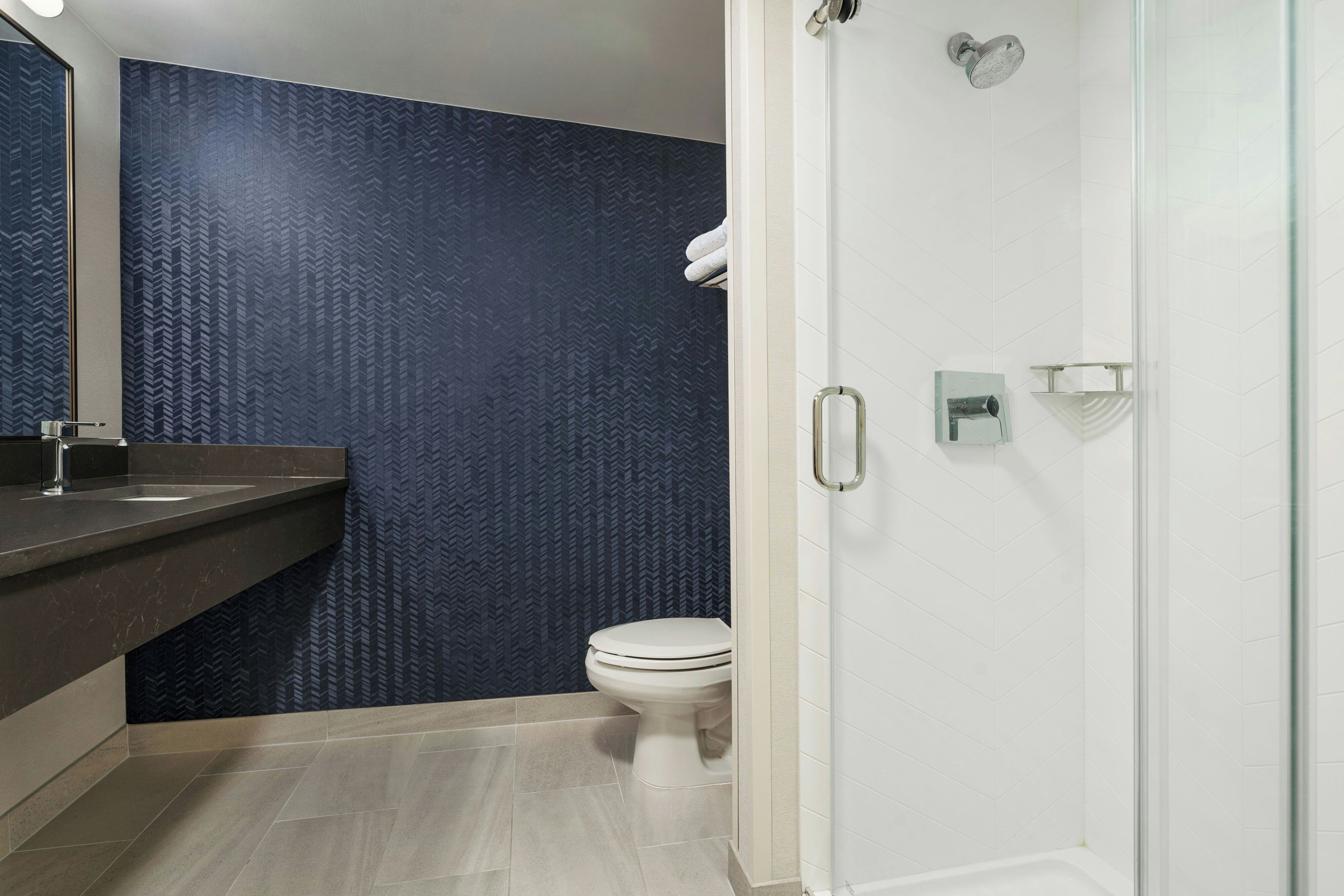 Une salle de bain au design moderne, avec un mur à motifs foncés, des toilettes blanches, une douche en verre et un comptoir en marbre avec un lavabo.