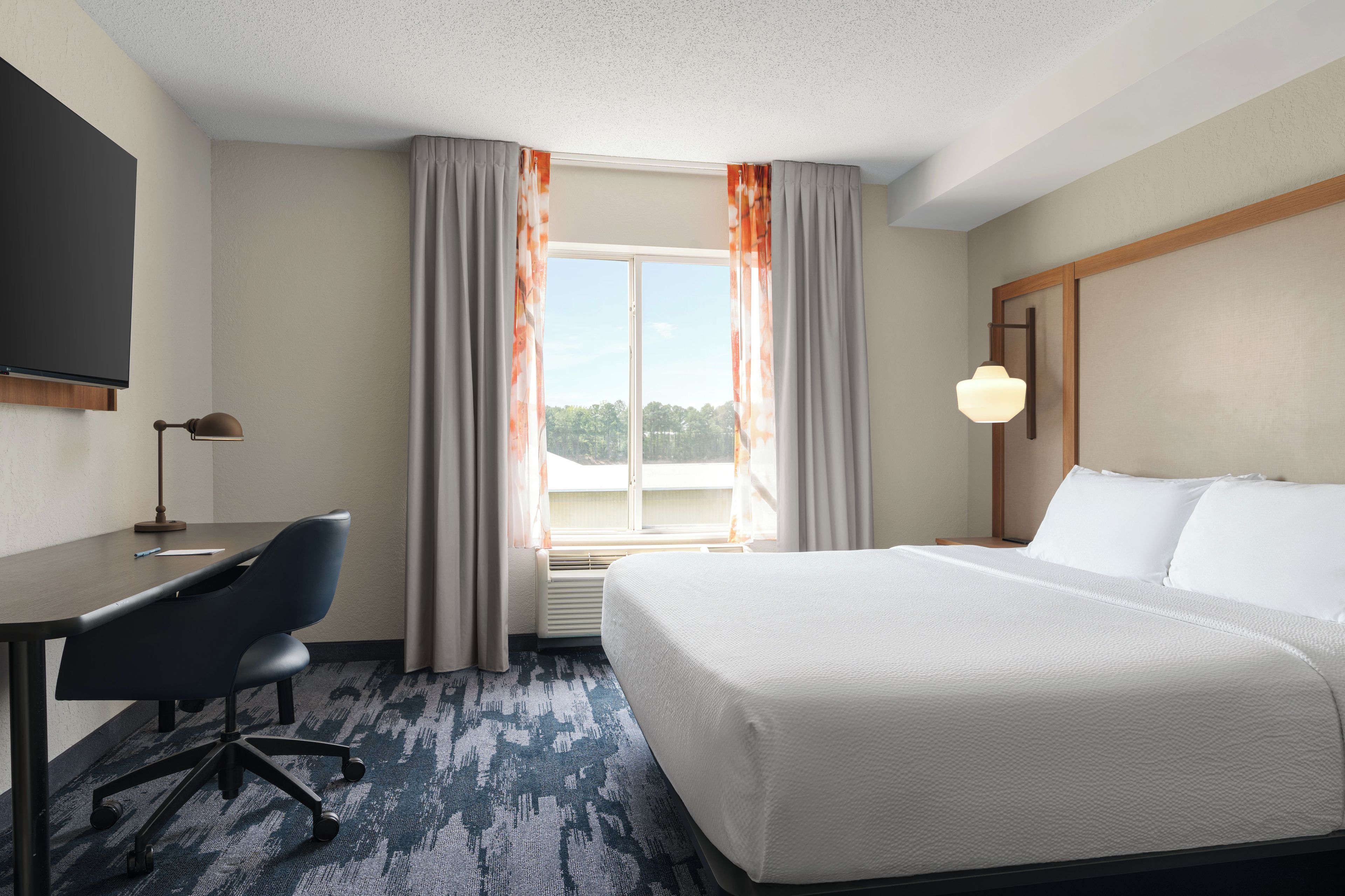 A hotel room with a bed, desk, chair, and a television.