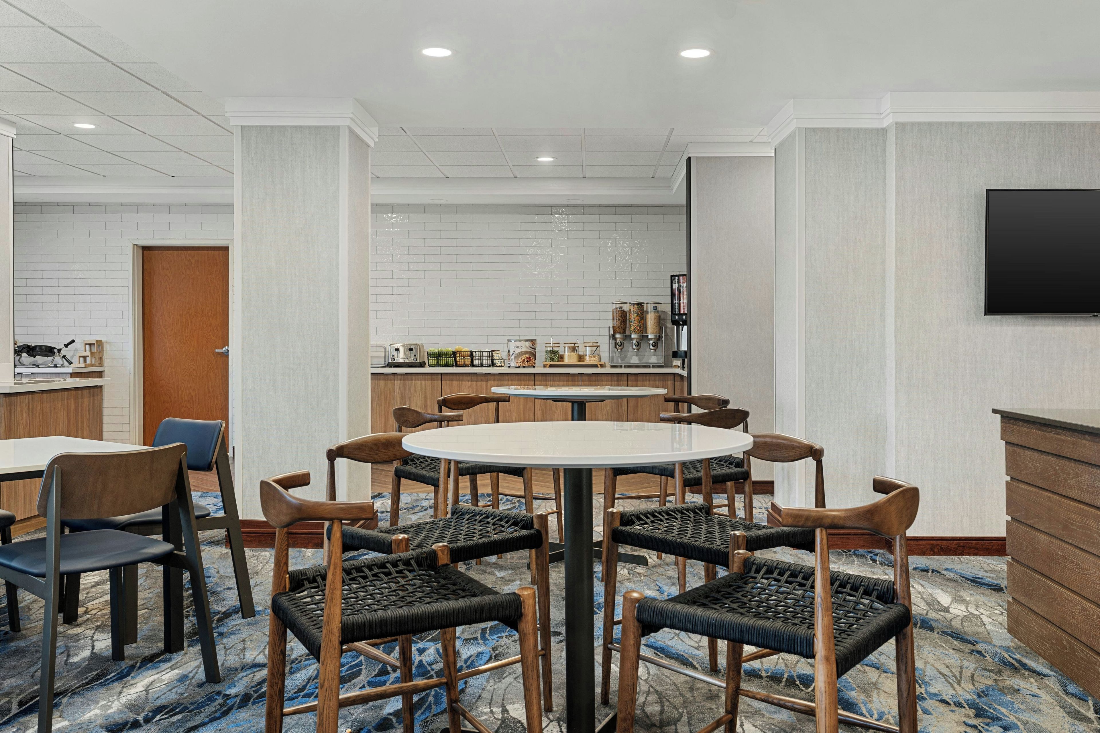 A hotel dining area with a round table, six chairs, a bar, and a television.