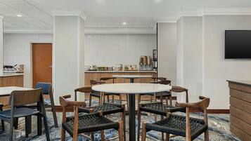 A hotel dining area with a round table, six chairs, a bar, and a television.