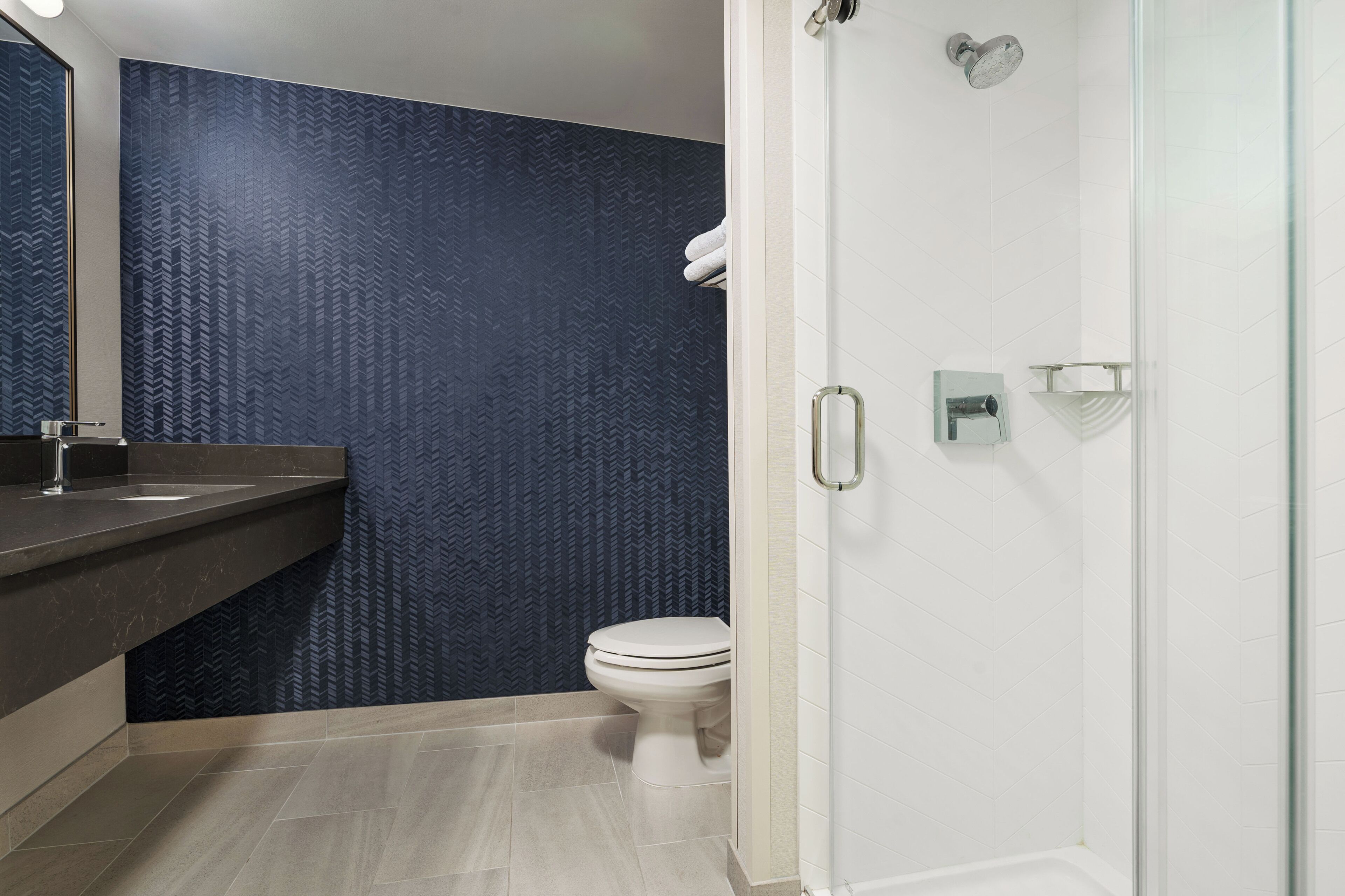 A modern bathroom with a dark patterned wall, a white toilet, a glass shower enclosure, and a marble countertop with a sink.