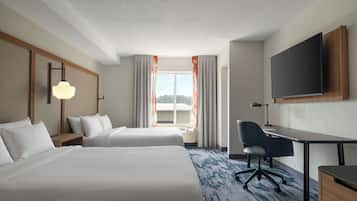 A hotel room with two beds, a desk, a chair, a TV, and a window with curtains.