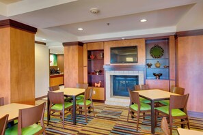 Un comedor de hotel con paredes de madera, una chimenea y sillas acolchadas verdes.