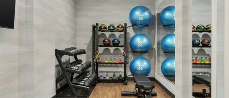 Un gimnasio con equipo de ejercicio, incluyendo mancuernas, una banca y pelotas de ejercicio.