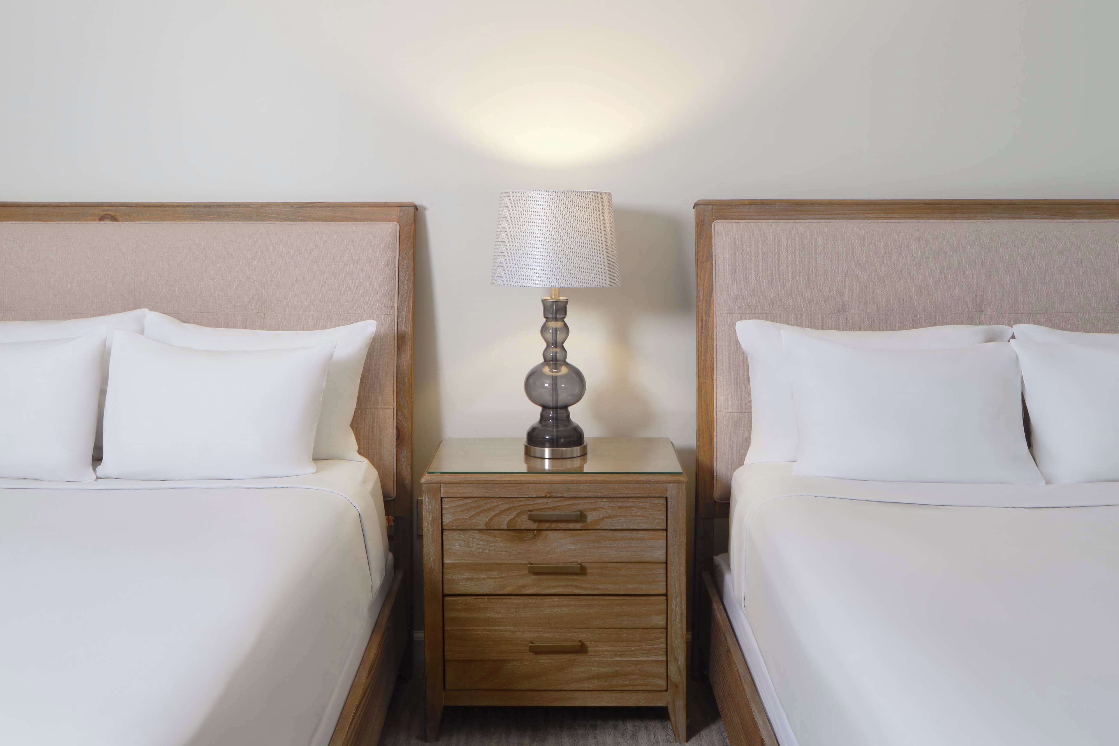 A hotel room with two beds, a nightstand with a lamp, and a drawer.