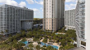 Un immeuble résidentiel de grande hauteur doté de nombreux balcons, d’une cour intérieure avec une piscine et d’un espace verdoyant environnant.