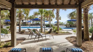 Un espace extérieur abrité, doté de chaises longues et de parasols, ainsi qu’une piscine et des palmiers.