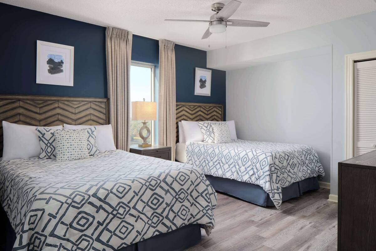 Une chambre d’hôtel avec deux lits, un ventilateur de plafond et une fenêtre avec des rideaux.