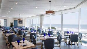 Un restaurant avec des tables et des chaises, de grandes fenêtres et une vue sur l’océan.