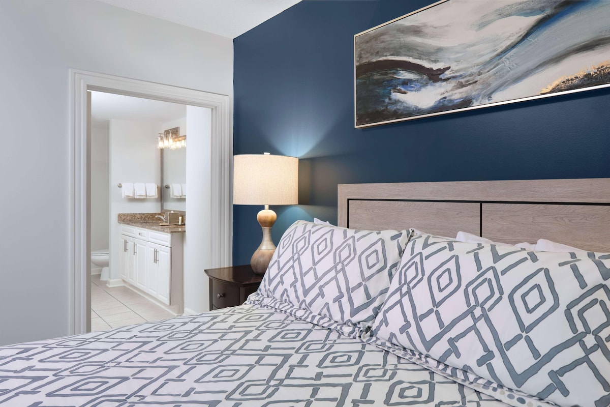A bedroom with a bed, a nightstand, a lamp, and a painting on the wall.